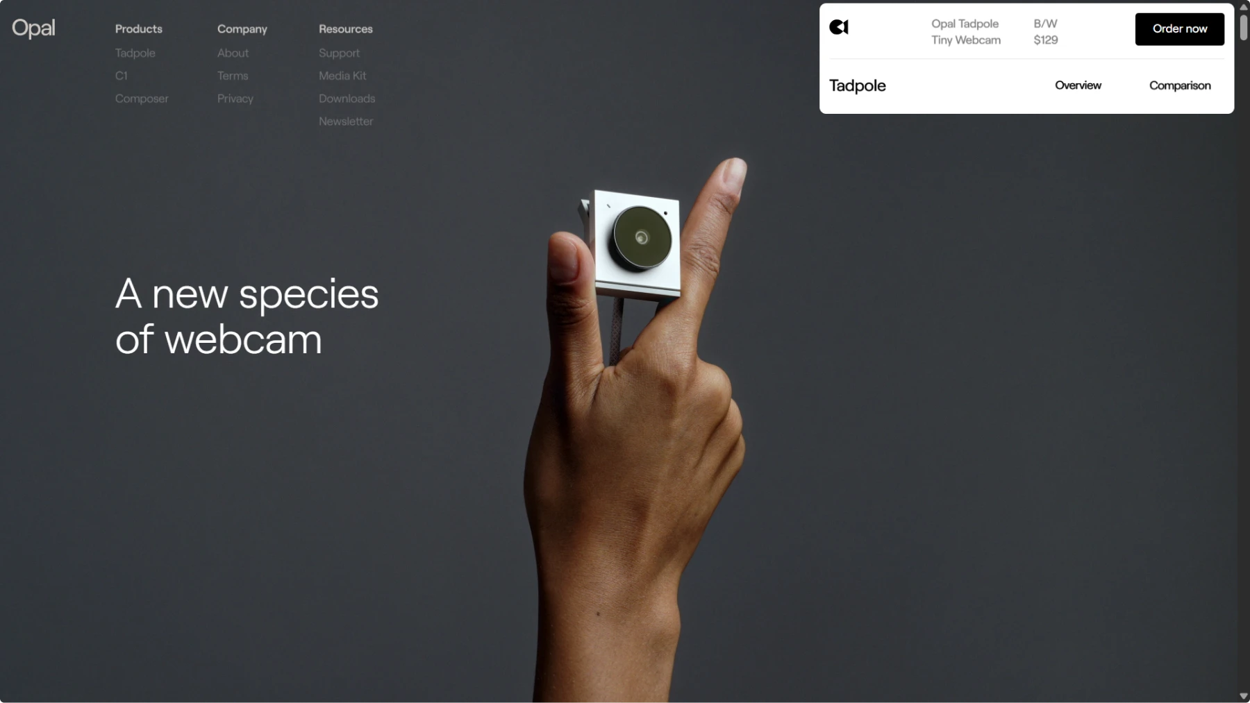 Screenshot of Opal Tadpole website showing a hand holding the tiny square webcam device against a dark background. Clean interface displays "A new species of webcam" headline with navigation menu and product details showing "$129" price. Minimal design emphasizes the product's compact size
